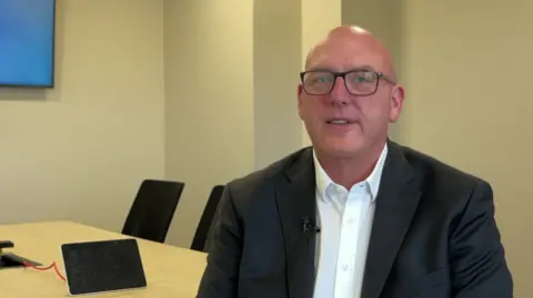 A man with black glasses wears a white shirt and black blazer