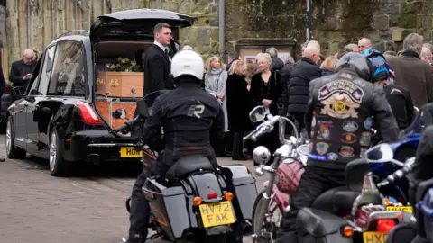 PA Media Harley Davidson riders gather behind the hearse to take part in a tribute following the funeral of DJ Johnnie Walker at St Peter's Church in Shaftesbury, Dorset. 