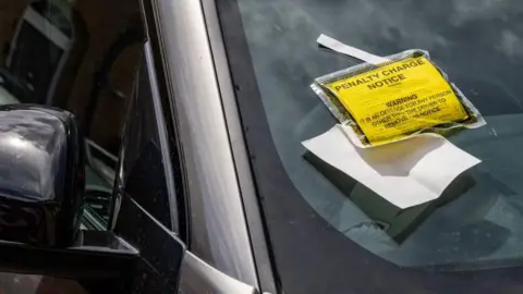 A Penalty Charge Notice (PCN) is pictured in the window of a vehicle on 27th June 2024 in Windsor, with a windshield to the left of the picture 