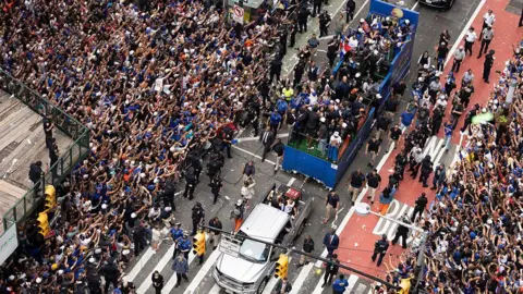 Getty Images crowds of fans holding their arms out toward a passing float