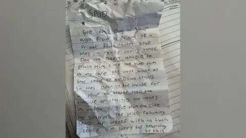 A handwritten note left with the dog reads: "Spud. Got this dog a year ago from a friend of a friend. His names Spud. He's a really loving house dog. I've been unable to train him since I've had him in my care. He won't walk on the lead or go down stairs so he's been living in the house for a year. He hasn't has the exercise or training he needs. I'm unable to give him the life he deserves. I've tried rehoming Spud for weeks with no luck. Really am sorry for resorting to this."