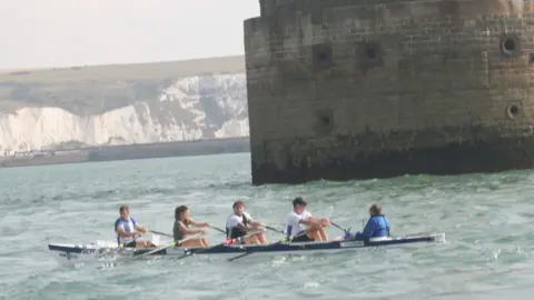 Handout Four rowers and a cox rowing on a body of water.