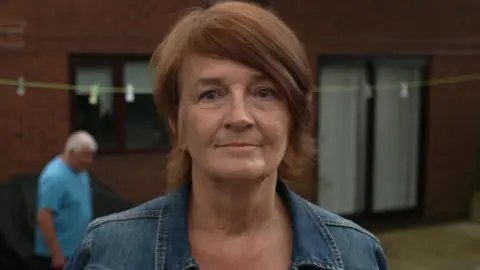 Woman with brown short hair and and a denim jacket stands outside
