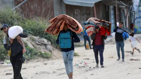 Four men carry belongings on their head and shoulders as they evacuate along a dirt track after an evacuation order in Beit Hanoun