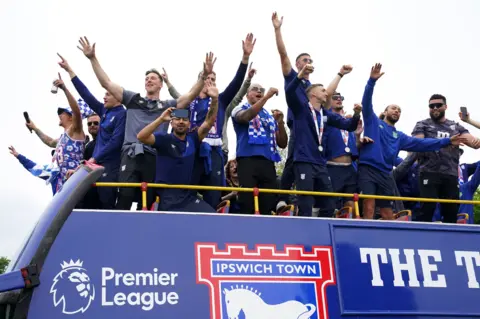 PA Ipswich Town players on the top of a double-decker promotion bus. 