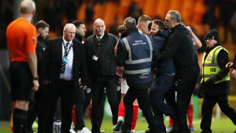 A Port Vale fan is escorted off the pitch by stewards and security in the home defeat by Portsmouth