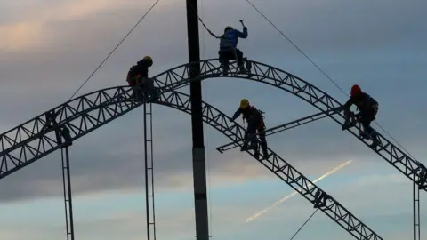 Reuters Construction workers are silhouetted against a pale blue sky as they start to set up a giant tent in Ciudad Juarez