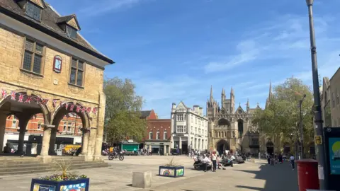 Joe Griffin/LDRS A view of the centre of Peterborough showing the cathedral in the background and people sitting in a paved square