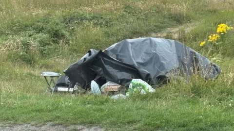 PD Ports A vehicle covered with tarpaulin and secured by bricks with a stool left outside. 