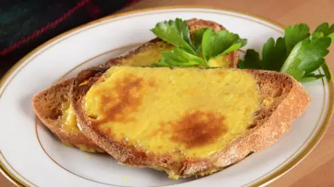A picture of Traditional Welsh rarebit. There are two slices of bread with some green garnish on the side.