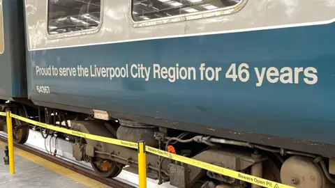 Side of a train featuring the wheels and the slogan Proud to serve the Liverpool City Region for 46 years