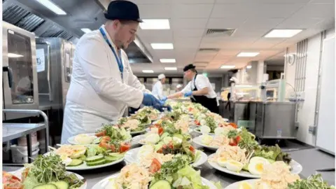 Qays Najm/BBC Cooking staff laying out lunch consisting of many plates of salad with eggs, lettuce and coleslaw.