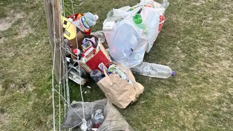 Shropshire Young Farmers Bags of rubbish, with some of it spilling out, on a grassy area beside a wire fence