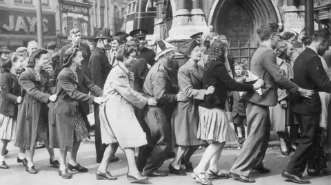 Getty Images Photo shows a line of a dozen people doing the conga smiling with police and crowds around