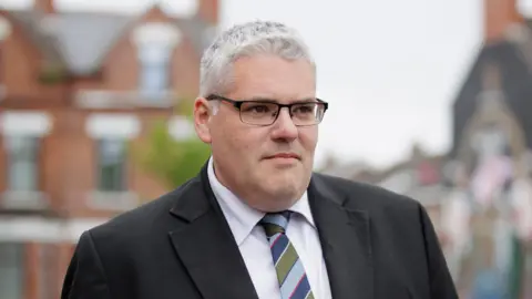 PA Media DUP leader Gavin Robinson, pictured in 2024. He has white hair, a grey suit and a stripey tie. 