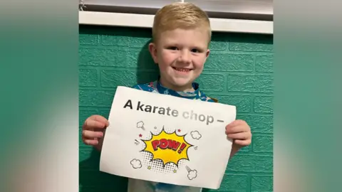 Cancer Research UK Stanley holding a white sign with black writing saying 'a karate chop'. Below it is a red comic book style 'pow'.