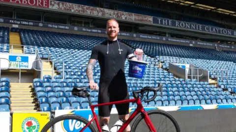 Lewis Robinson Lewis Robinson stands with his bike in Blackburn Rovers' Ewood Park stadium holding a charity collection bucket