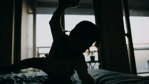 Getty Images A silhouette image of a child crawling across a bed with one arm raised as if to hit out. The rest of the room is blurred in the background.