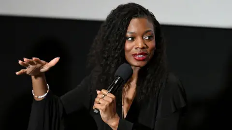 Nia DaCosta gesturing as she speaks into a microphone 