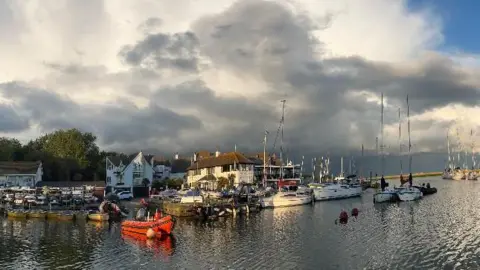 Ant Black and white clouds mingle over boats moored on the river in Christchurch