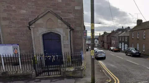 Google a church sits at the end of a road which has cars parked on both sides in front of houses