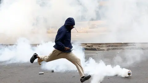 THOMAS MUKOYA / REUTERS A man shields his face and runs away from a tear gas canister.