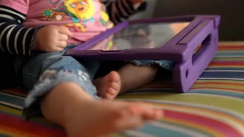 A unidentifiable toddler playing on a table in a purple case