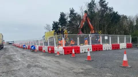 Lots of men in high vis jackets digging a road