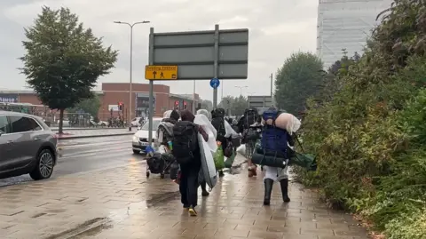 People walking, with their backs to the camera, to the festival site, close to Reading station, with The Range store on the left of the picture.
