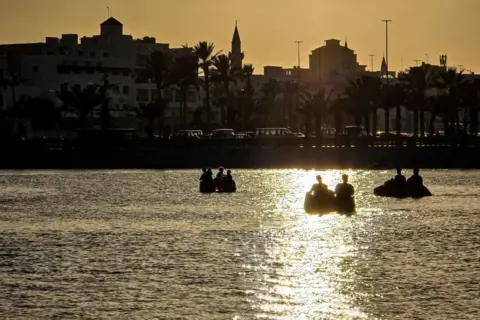 MAHMUD TURKIA/AFP People sit in boats in the artificial Saraya Museum Lake by the Martyrs' Square. The sun is setting behind them.