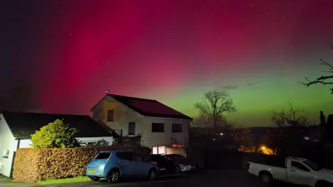 GDW/BBC Weather Watchers A scarlet, pink and green-toned sky with houses and cars seen in the foreground in Dartington, Devon.