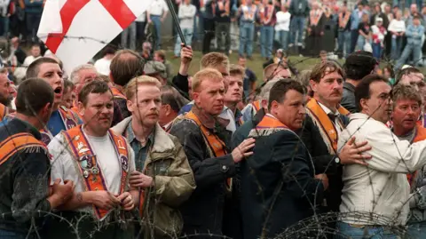 Pacemaker Members of the Orange Order stand behind barbed wire. 