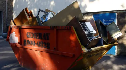 BBC A skip full of woods, doors, furniture and other rubbish.