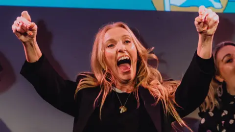 Collete on stage in a black jacket punches two fists in the air