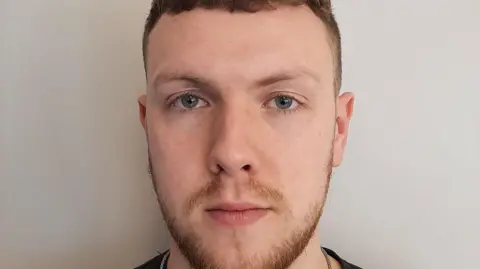 Custody picture of Benjamin Bottomley, a young man with a short beard. 