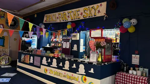 HANNAH CRAMP A snack shop counter stocked with sweets, popcorn and drinks in a cinema foyer is decorated with colourful bunting, balloons and lights - as well as hand-painted banners showing Toy Story slogans 'To infinity and beyond' and 'REACH FOR THE SKY', and themed props.