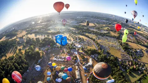 Paul Box An aerial view of the entire Bristol Balloon Fiesta site showing parking areas, the crowd and dozens of balloons either in flight or about to take off