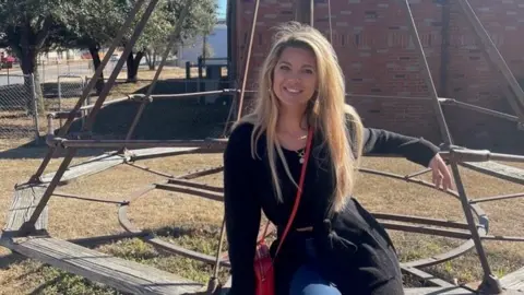 Adrienne Martin sits on a bench outside while wearing a black sweater