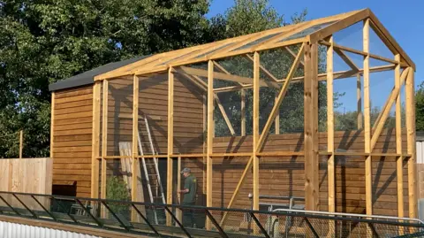 Luke Deal/BBC A picture of one of the red squirrel enclosures that is currently being built. It shows a large wooden structure with wire panels in place. A worker can be seen inside the enclosure helping with construction.