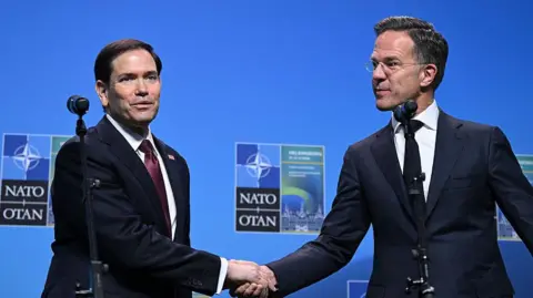 Nato Secretary General Mark Rutte (R) and US Secretary of State Marco Rubio shake hands in front of a blue Nato backdrop