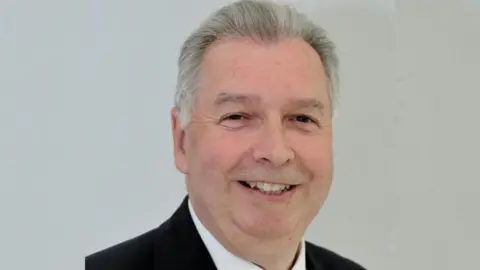 Dexter Smith's leader picture, with him smiling and wearing a dark suit.