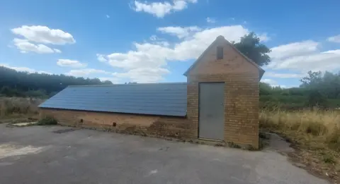 Bournemouth Water/South West Water A long brick building that rises only half a storey from the ground with a large pitched tiled roof. The building has a taller section at one end with a grey door, presumably leading to some stairs below ground.