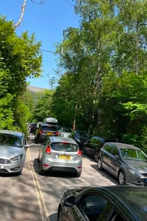 Tabitha Cars parked on either side of the road. There is stationary traffic in the middle of the road. 