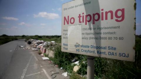 Sign warning people not to fly tip in Bexley, with long pile of rubbish behind it
