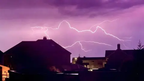 Roger Turner Fork lightning in a purple sky above sillhoutted houses