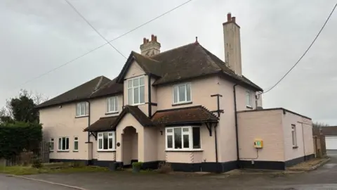 Brian Farmer/BBC A large pink painted building with white-framed windows and a red-tiled roof.