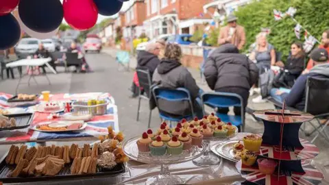 Getty Images A table of sandwiches and cake is decorated with Union flags and people are sitting round a table holding a street party outside. Bunting has also been put up.
