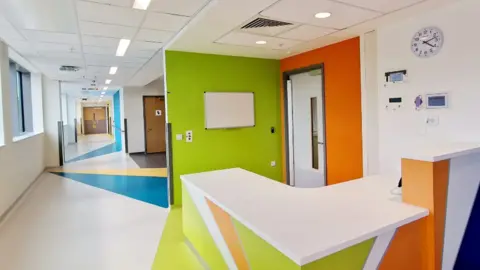 Sandwell and West Birmingham NHS Trust The inside of a hospital building, with bright colours on the walls and floors and welcome desk