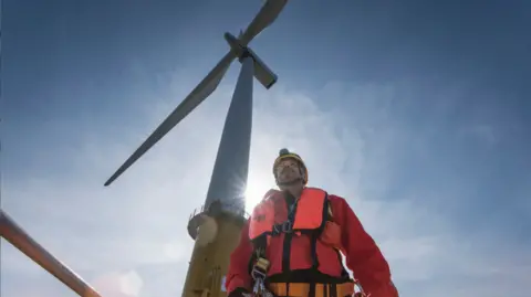 Getty Images Man stands below offshore turbine rising into sky