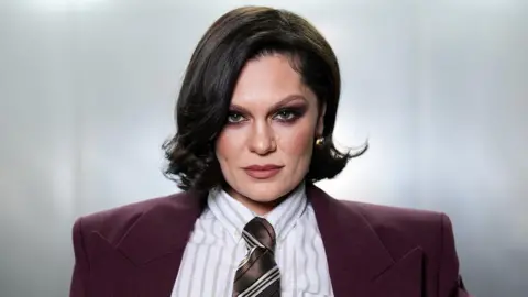 Jessie J looking straight at the camera while wearing a suit and tie